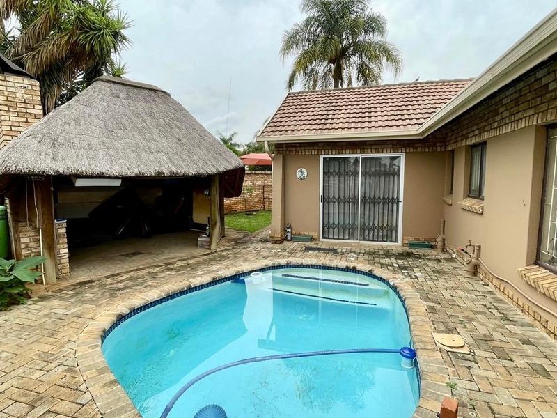 Outdoor entertainment area featuring a swimming pool, brick-paved patio, and a traditional thatched lapa structure adjacent to the main house.