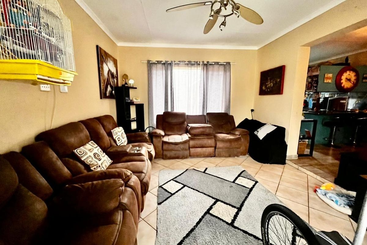 A comfortable living room featuring tiled flooring and a ceiling fan, with an open-plan layout connecting to the adjacent kitchen area.
