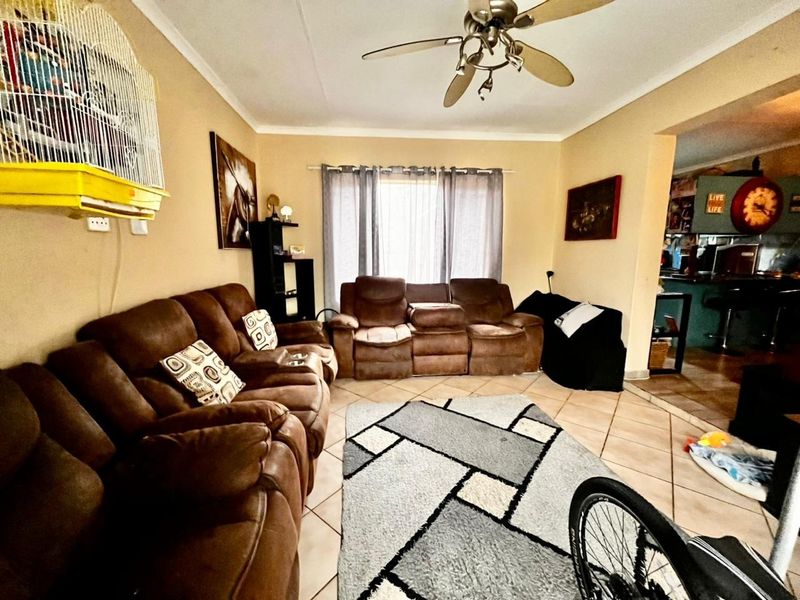 A comfortable living room featuring tiled flooring and a ceiling fan, with an open-plan layout connecting to the adjacent kitchen area.