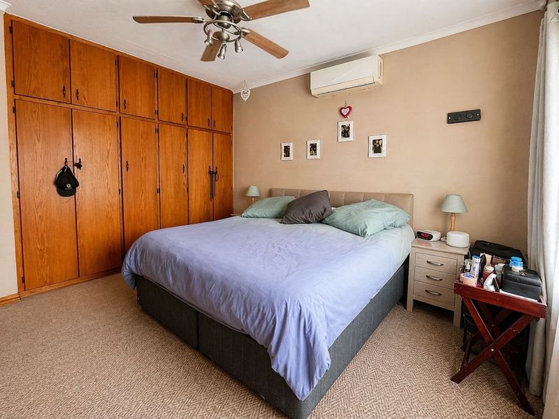 A bedroom featuring built-in wooden cabinetry, a ceiling fan, and a wall-mounted air conditioning unit.