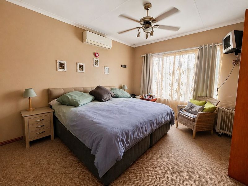 A carpeted bedroom featuring a ceiling fan, split-system air conditioning unit, and large window with curtain tracks.