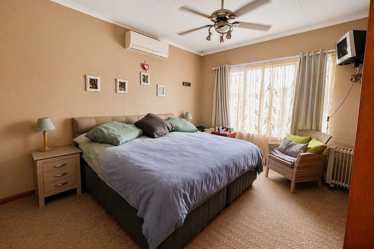 A carpeted bedroom featuring a ceiling fan, split-system air conditioning unit, and large window with curtain tracks.