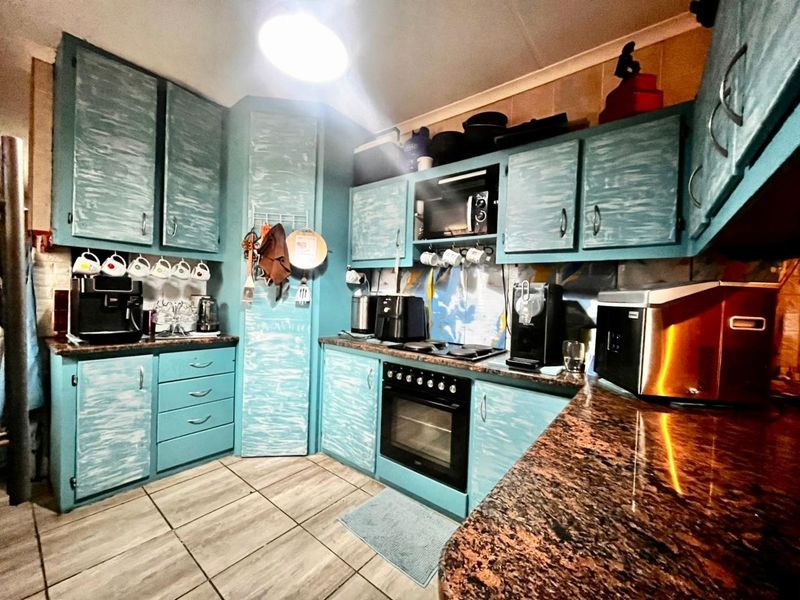 A functional kitchen featuring blue painted cabinetry, granite countertops, and built-in cooking appliances with tiled flooring and backsplash.