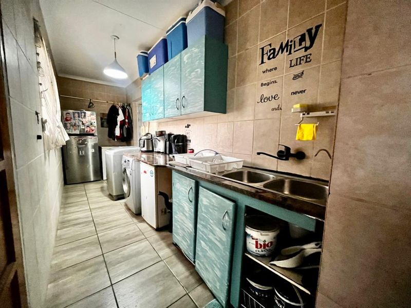 Functional laundry area featuring a double stainless steel sink, tiled splashback, and built-in cabinetry with ample storage space.
