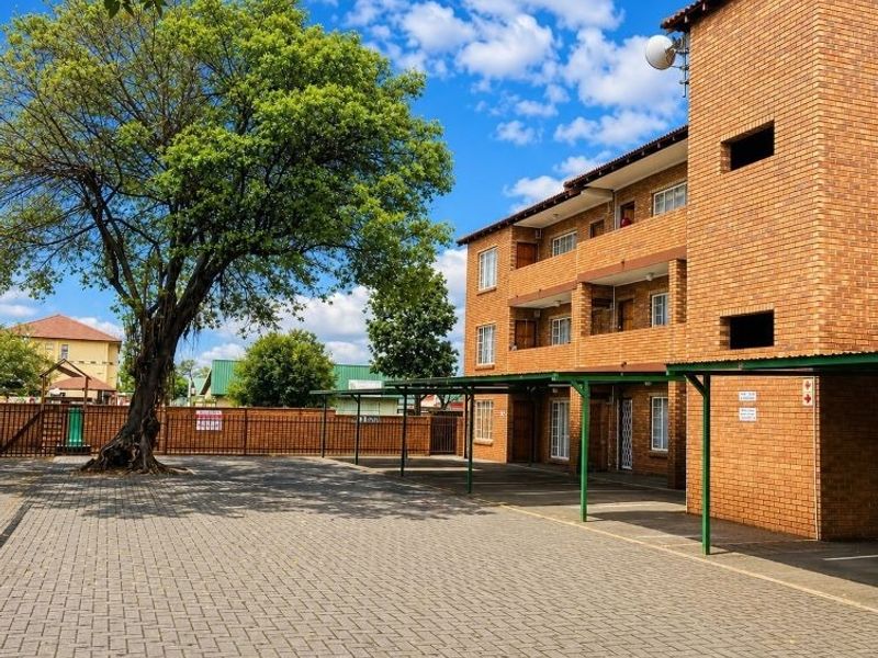 Exterior view of a multi-story brick apartment complex featuring covered parking bays, paved driveway, and private balconies.