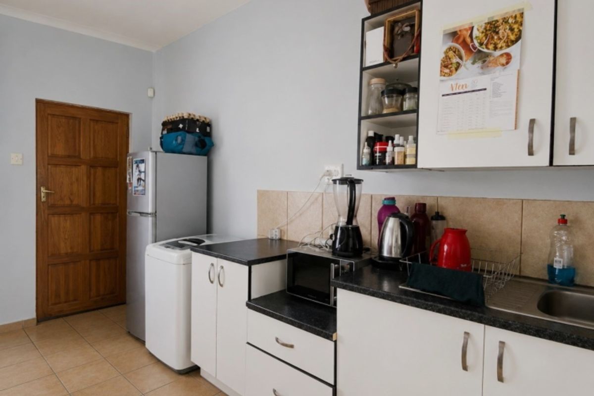 A functional kitchen featuring white cabinetry, dark laminate countertops, tiled backsplash, and tiled flooring, with an adjacent wooden door.