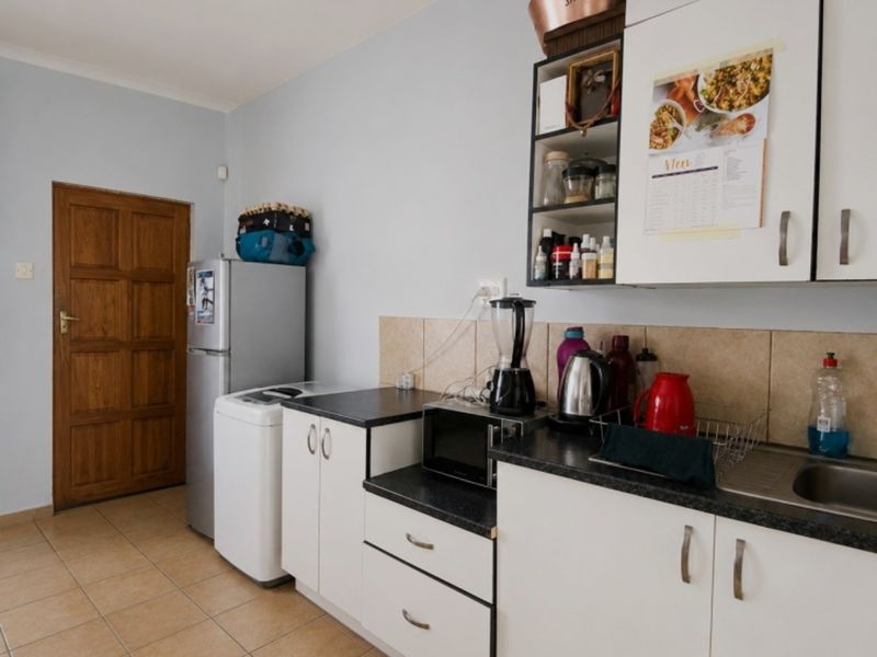 A functional kitchen featuring white cabinetry, dark laminate countertops, tiled backsplash, and tiled flooring, with an adjacent wooden door.