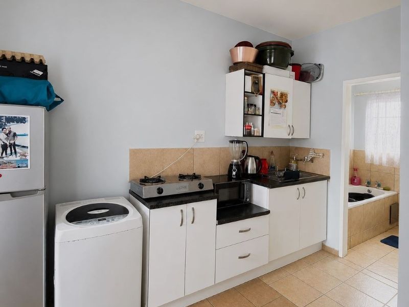 Compact kitchen featuring white cabinetry, dark countertops, tiled backsplash, and a gas hob, with an adjacent bathroom visible through the doorway.