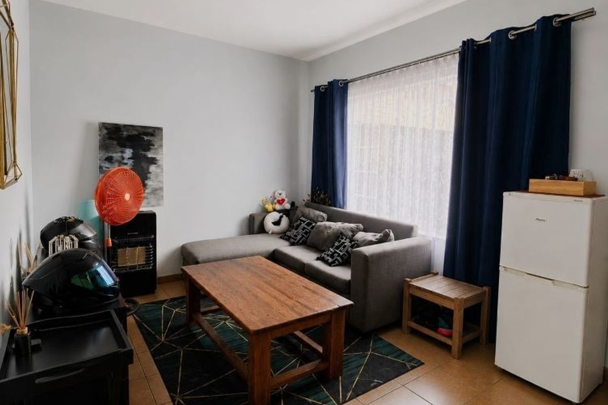 A living room featuring tiled flooring and a large window with curtain rods, providing a functional space for relaxation.