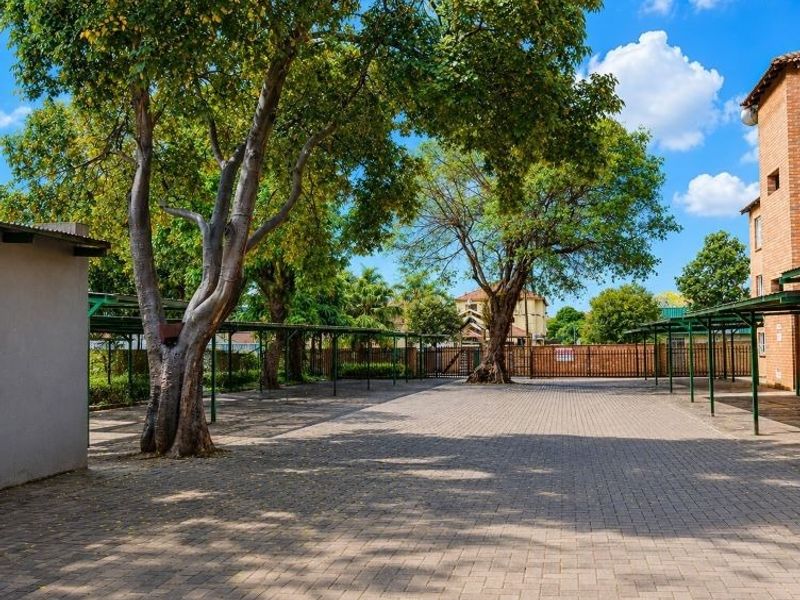 A well-maintained paved parking area featuring covered bays, mature trees, and brick building facades within an apartment complex.