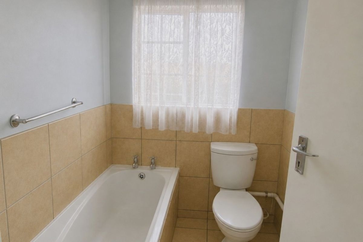 A functional bathroom featuring a bathtub, toilet, and neutral tiled finishes, offering a clean and simple layout.