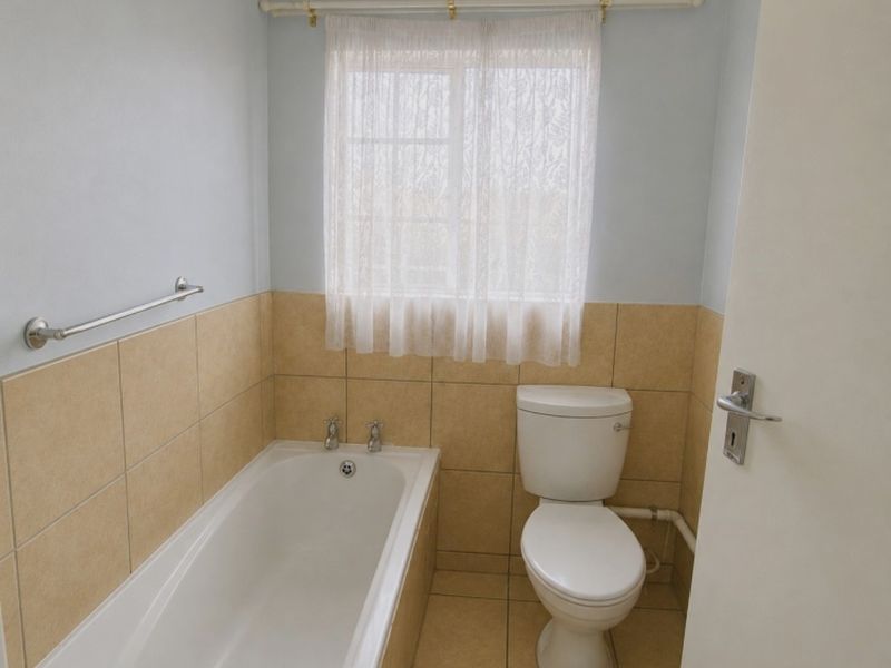 A functional bathroom featuring a bathtub, toilet, and neutral tiled finishes, offering a clean and simple layout.
