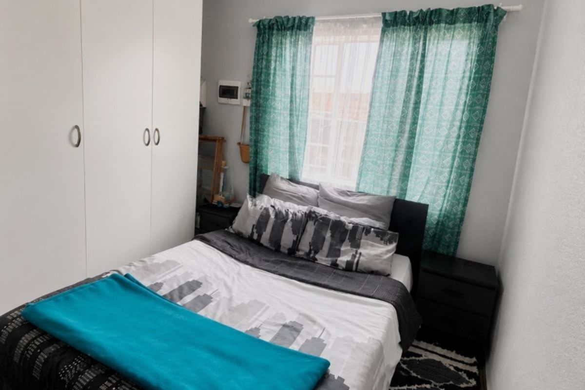 A compact bedroom featuring a built-in wardrobe with white cabinetry and a window with natural light.