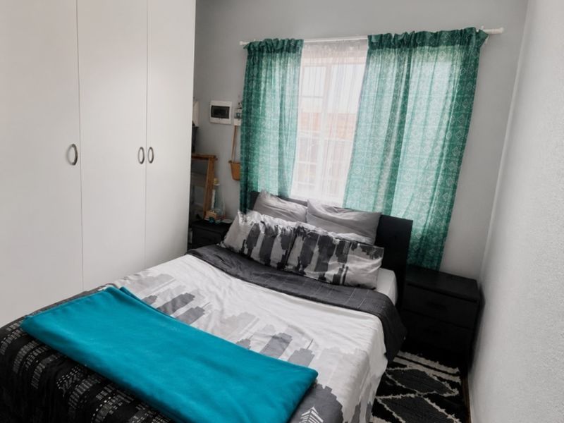 A compact bedroom featuring a built-in wardrobe with white cabinetry and a window with natural light.