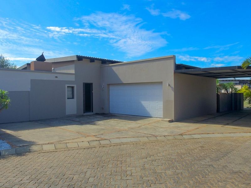 Front exterior view of a modern house featuring a single garage, attached carport, and a paved driveway.