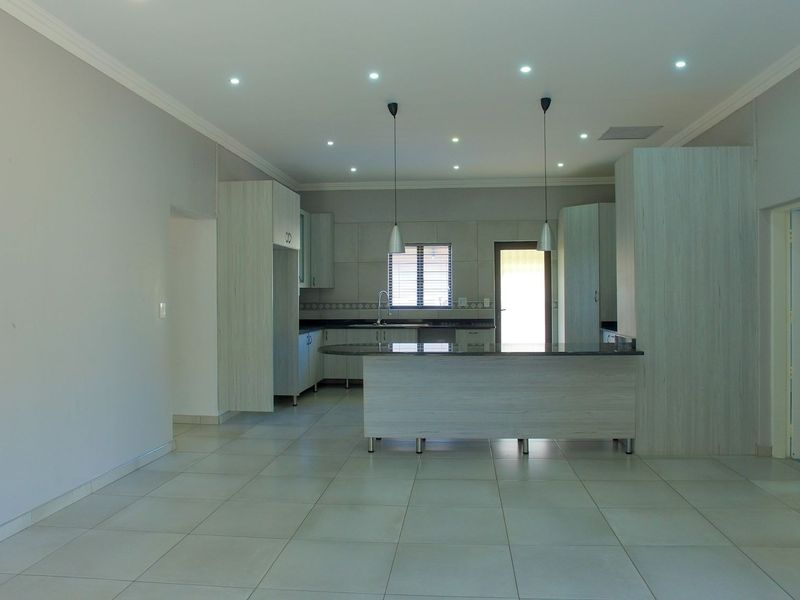 Spacious open-plan kitchen and living area featuring modern cabinetry, a breakfast bar, stone feature wall, and neutral tiled flooring throughout.