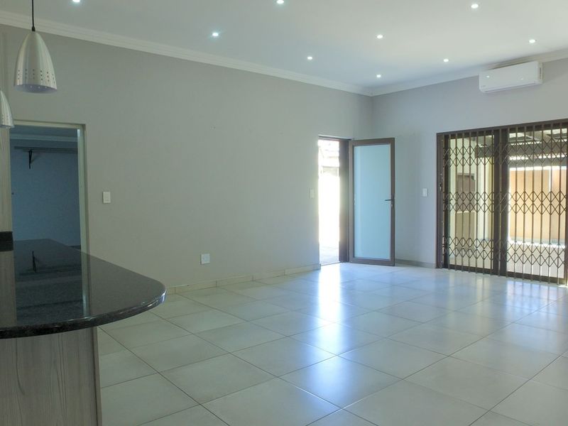 Spacious open-plan living area featuring tiled floors, recessed lighting, a granite breakfast bar, and direct access to the exterior through a security gate.