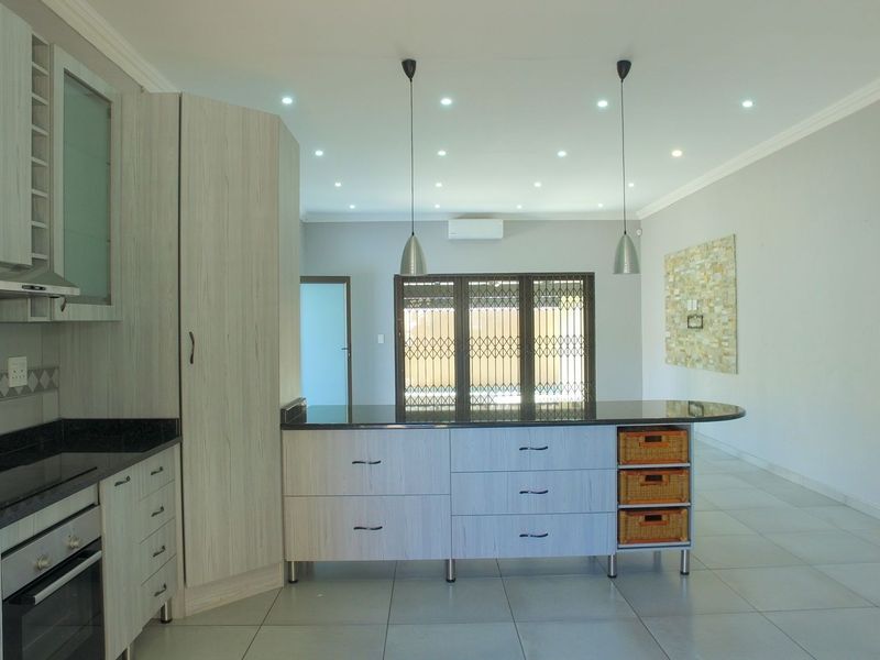 Modern open-plan kitchen featuring light wood cabinetry, granite countertops, a central island, and recessed lighting, flowing into a spacious living area.