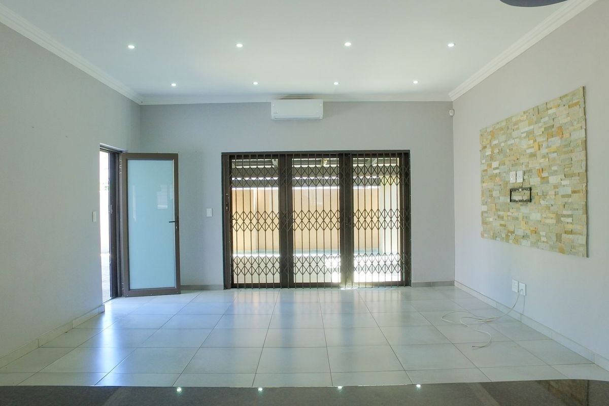 Spacious, light-filled living area featuring neutral tiled flooring, a stone accent wall, recessed lighting, and a split-system air conditioner.