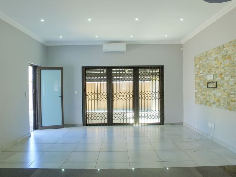 Spacious, light-filled living area featuring neutral tiled flooring, a stone accent wall, recessed lighting, and a split-system air conditioner.