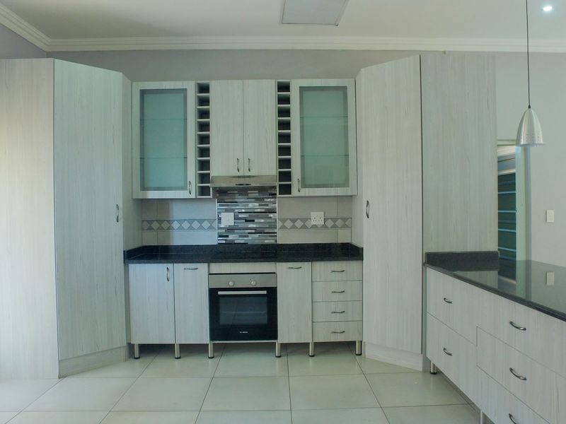 Modern kitchen featuring light wood-grain cabinetry, dark granite countertops, built-in oven, extractor fan, and stylish mosaic tile backsplash with neutral floor tiles.