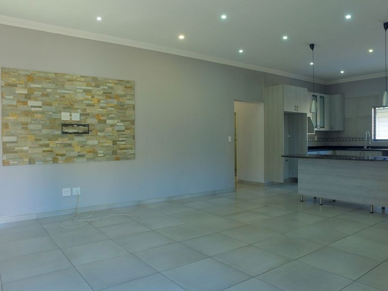 Spacious open-plan living and kitchen area featuring a stone accent wall, modern cabinetry, granite countertops, and neutral tiled flooring throughout.