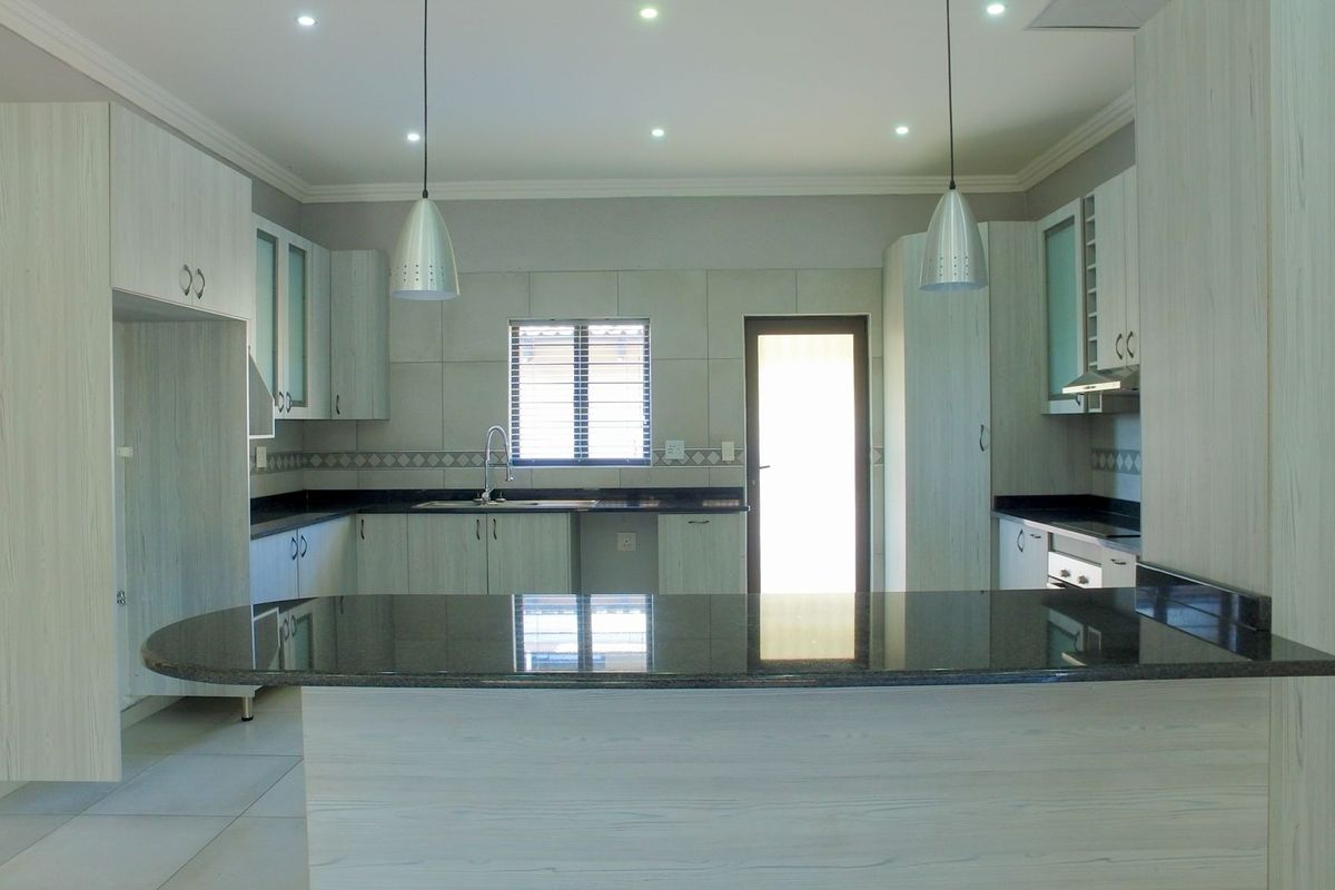 Modern kitchen featuring light wood-grain cabinetry, dark granite countertops, a central island, and integrated lighting, offering a clean and functional workspace.