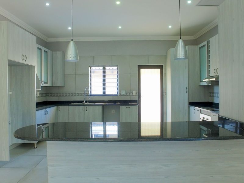 Modern kitchen featuring light wood-grain cabinetry, dark granite countertops, a central island, and integrated lighting, offering a clean and functional workspace.