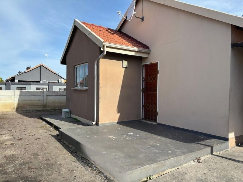 Rear view of the house featuring a concrete patio area, security gate, and tiled roof structure.