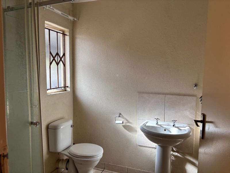 A functional bathroom featuring a pedestal basin, toilet, and shower enclosure, requiring cosmetic updates to improve its overall condition and aesthetic appeal.