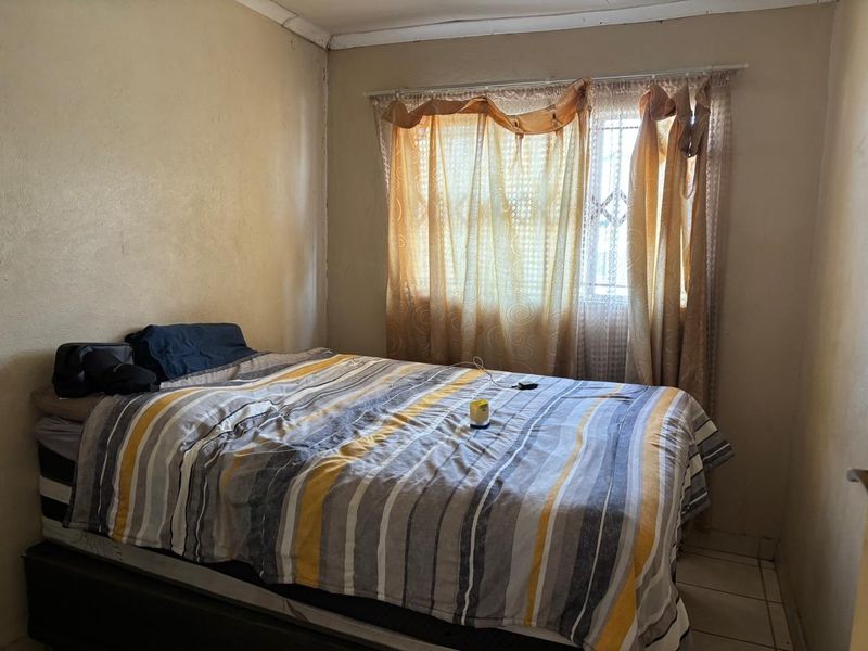 A bedroom featuring tiled flooring and a window with a security gate, requiring cosmetic updates to the wall finishes.