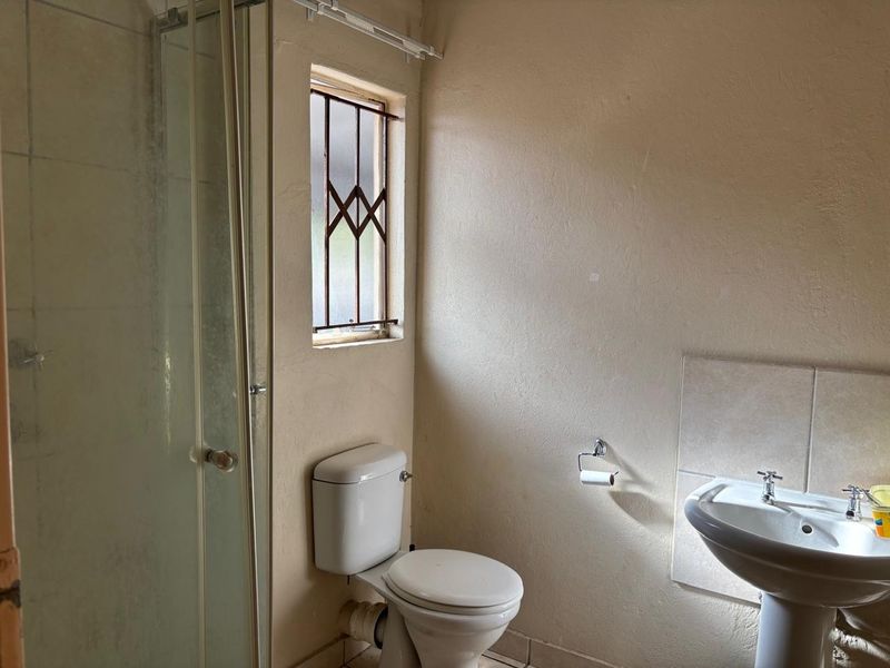 A functional bathroom featuring a shower enclosure, pedestal basin, and toilet, with security bars on the window.