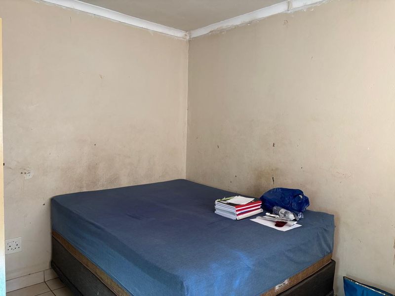 A bedroom featuring plain walls with visible surface wear and staining, requiring cosmetic updates to improve the overall condition of the space.