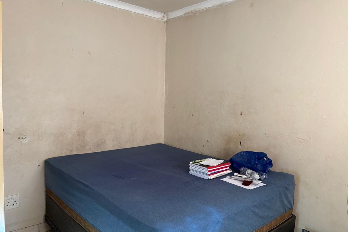 A bedroom featuring plain walls with visible surface wear and staining, requiring cosmetic updates to improve the overall condition of the space.