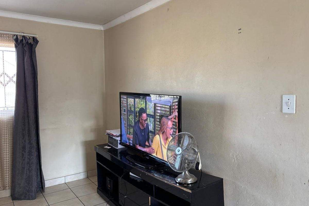 A living room area featuring ceramic floor tiles, coved ceiling cornices, and neutral wall finishes, providing a functional space for relaxation.