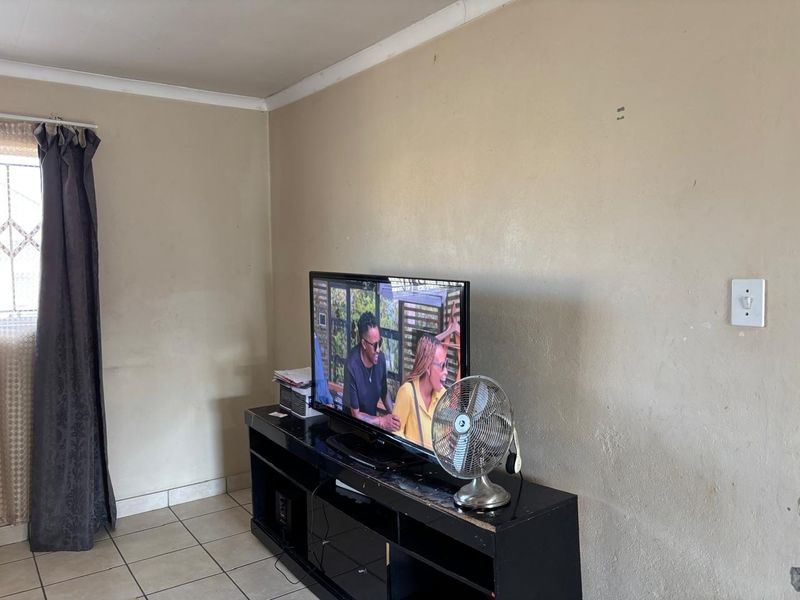 A living room area featuring ceramic floor tiles, coved ceiling cornices, and neutral wall finishes, providing a functional space for relaxation.