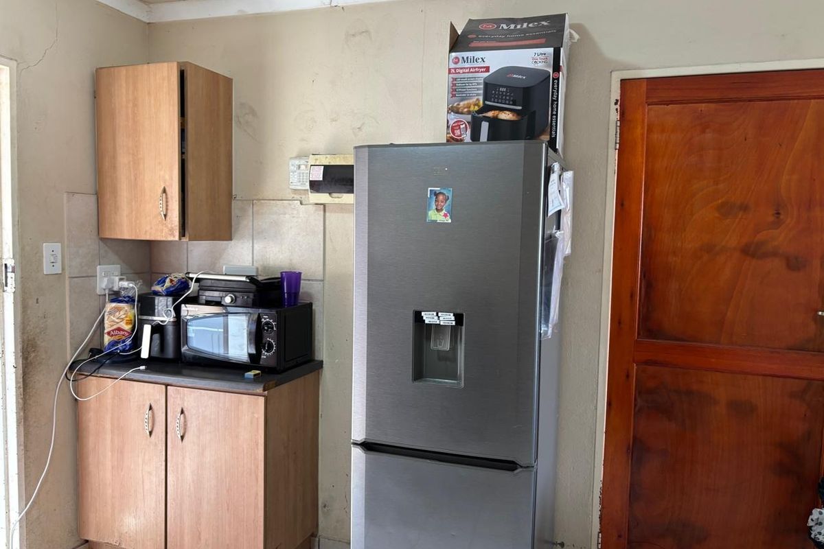 A compact kitchen area featuring laminate cabinetry, tiled splashbacks, and a timber door, currently showing signs of wear and requiring cosmetic maintenance.