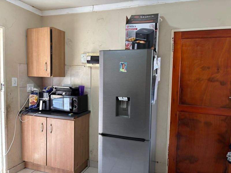 A compact kitchen area featuring laminate cabinetry, tiled splashbacks, and a timber door, currently showing signs of wear and requiring cosmetic maintenance.
