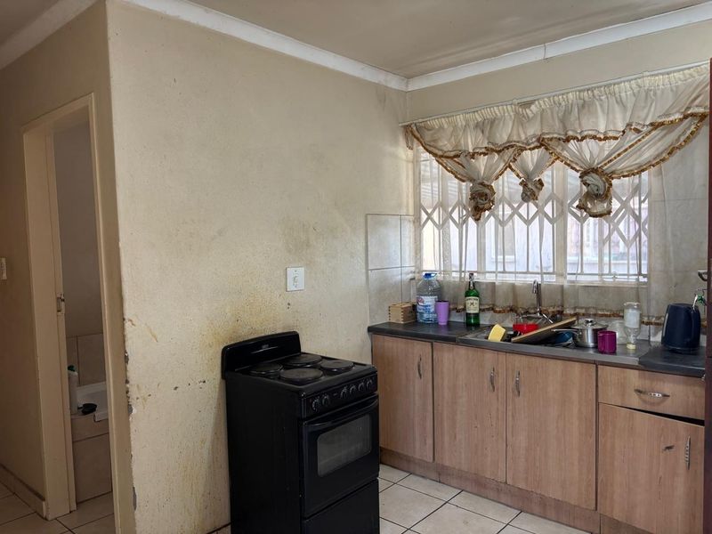 A dated kitchen featuring wood-look cabinetry, a stainless steel sink, and a freestanding stove, requiring cosmetic updates and wall refinishing.