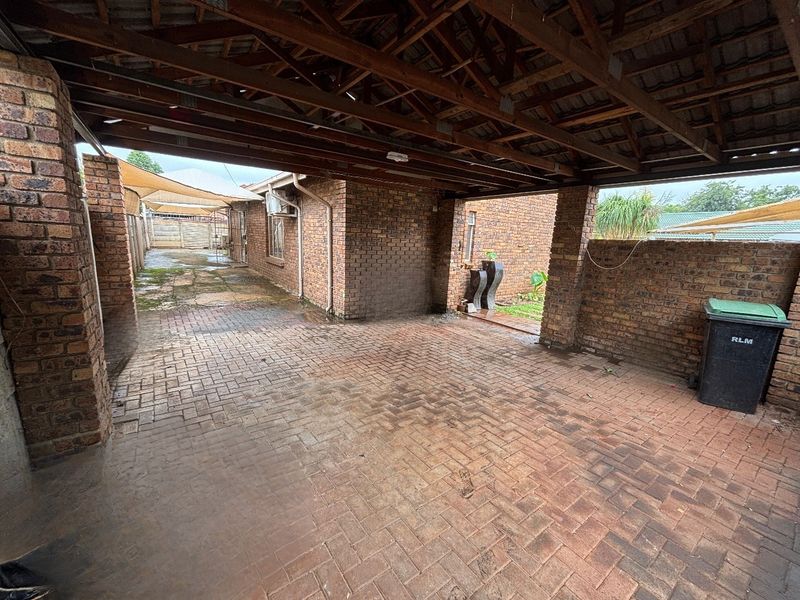 A spacious covered carport featuring exposed timber roof trusses and durable brick paving, providing functional off-street parking.
