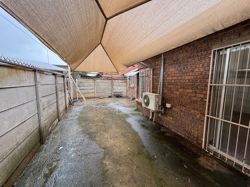 A paved outdoor patio area featuring a large shade sail, brick exterior walls, and an installed air conditioning unit.