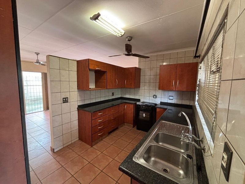 A functional kitchen featuring dark wood cabinetry, granite countertops, a double basin sink, and tiled finishes throughout.