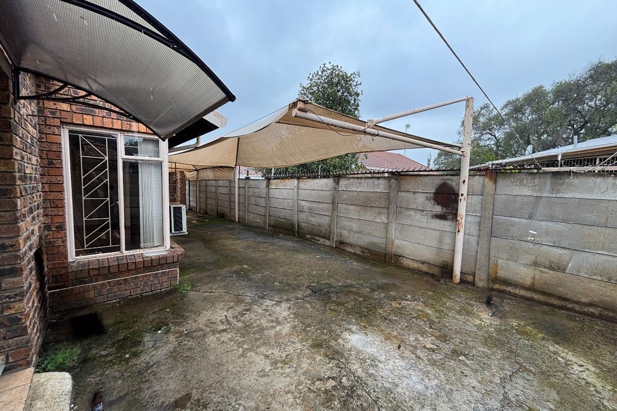 Rear exterior area featuring concrete paving, a shade sail structure, and perimeter precast concrete walling, requiring maintenance and surface cleaning.