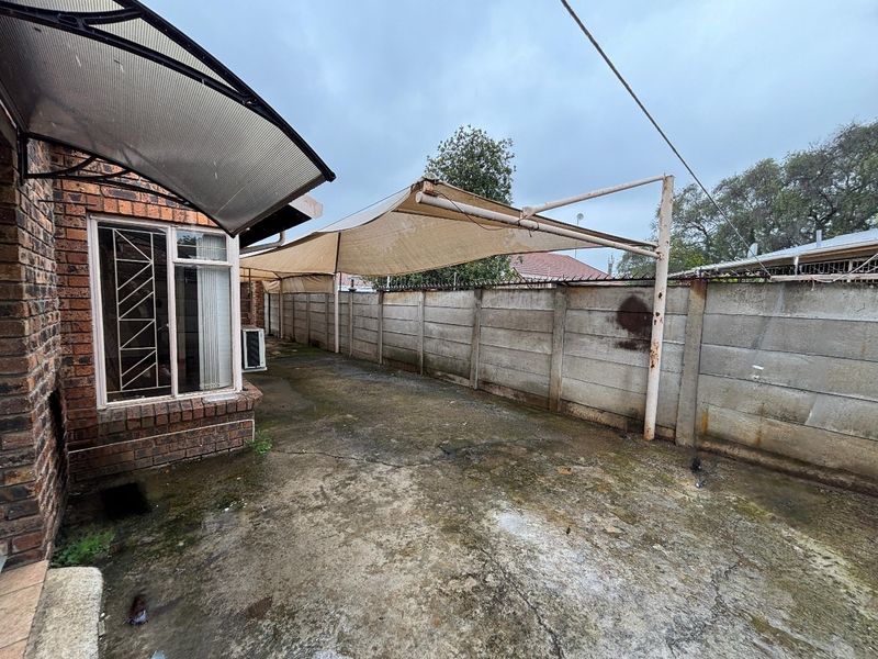 Rear exterior area featuring concrete paving, a shade sail structure, and perimeter precast concrete walling, requiring maintenance and surface cleaning.