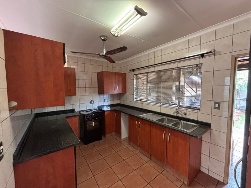 A functional kitchen featuring wooden cabinetry, granite countertops, a double sink, and tiled finishes, offering a practical layout ready for modernization.