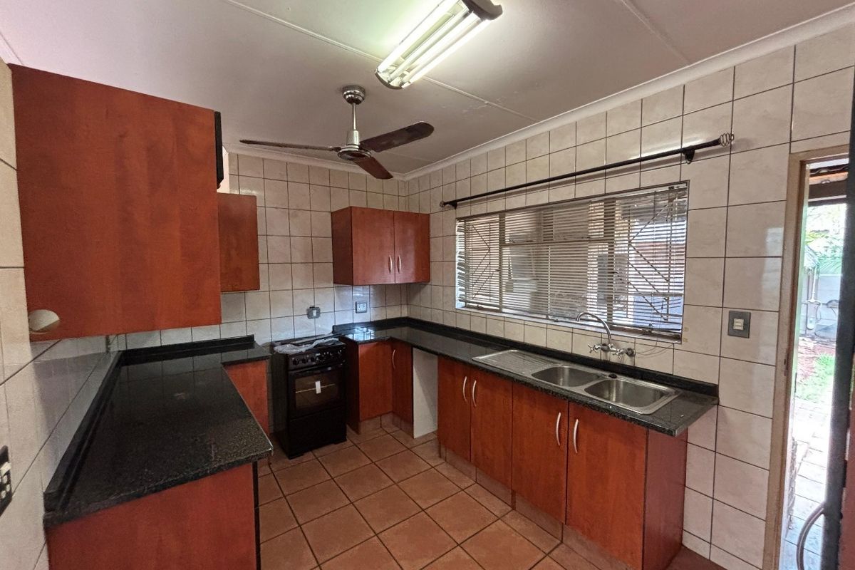 A functional kitchen featuring wooden cabinetry, granite countertops, a double sink, and tiled finishes, offering a practical layout ready for modernization.
