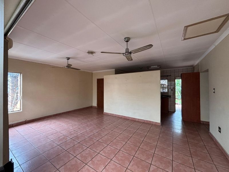 Spacious open-plan living area featuring tiled flooring, dual ceiling fans, and neutral wall finishes, offering a blank canvas for renovation.