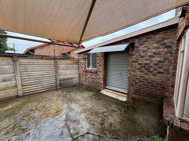 Outdoor patio area featuring brick construction, a roller shutter door, and a shade sail, with concrete paving requiring maintenance.