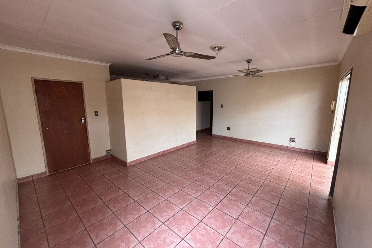 Spacious, empty living area featuring tiled flooring, ceiling fans, and an air conditioning unit, offering a blank canvas for interior design.