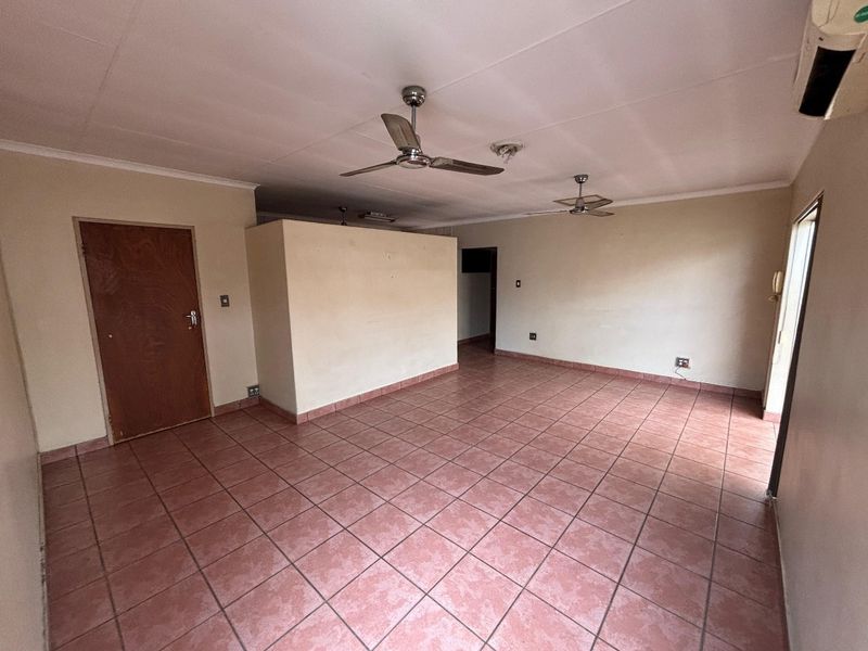 Spacious, empty living area featuring tiled flooring, ceiling fans, and an air conditioning unit, offering a blank canvas for interior design.
